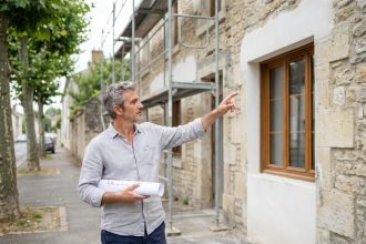 Architecte devant une façade de maison en rénovation avec nouvelles fenêtres en bois et ravalement partiel