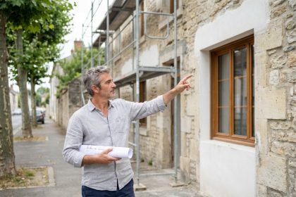 Architecte devant une façade de maison en rénovation avec nouvelles fenêtres en bois et ravalement partiel
