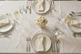 Vue de dessus d'un couvert formel avec verres à vin, à eau et flûtes à champagne correctement positionnés sur nappe blanche